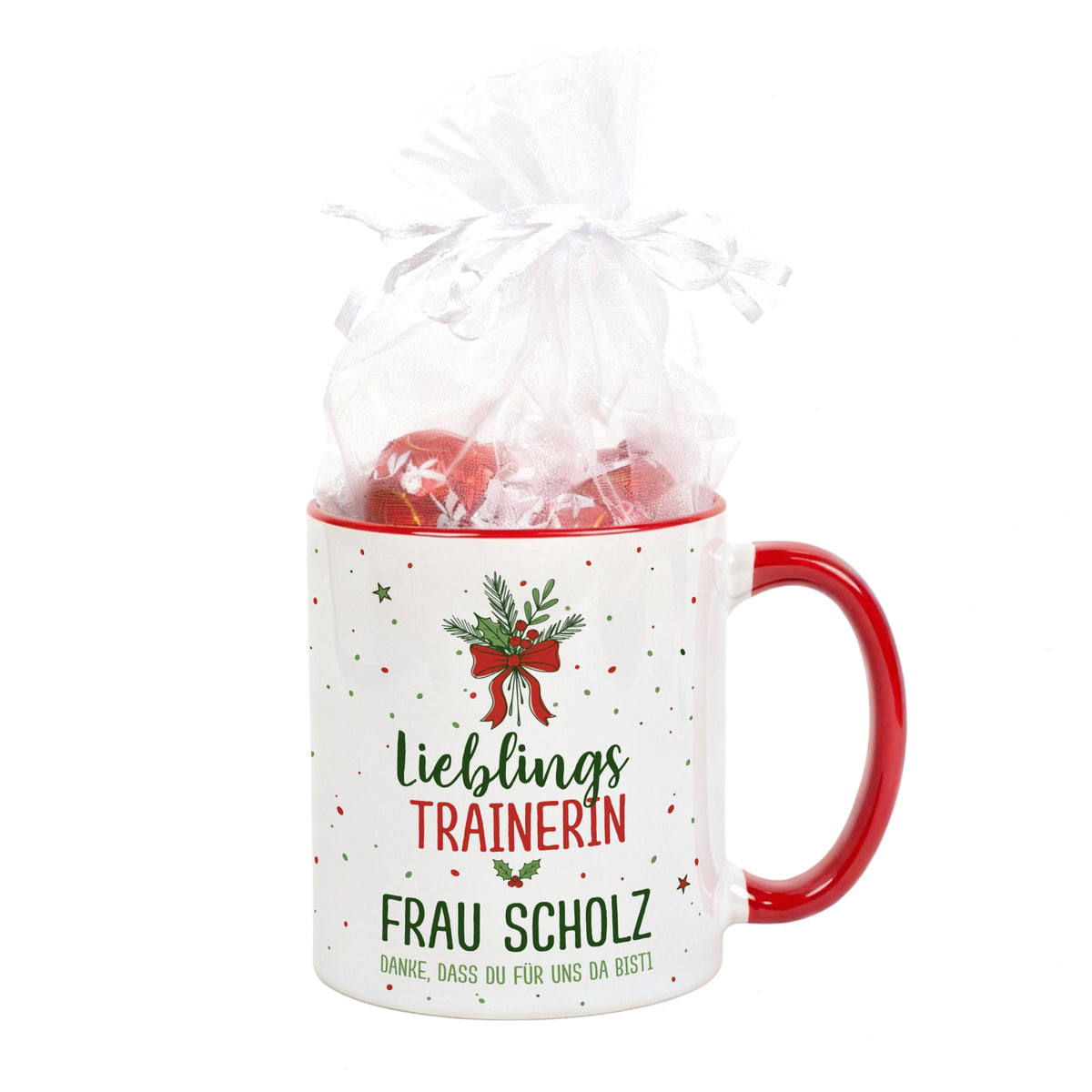 Personalisierte Weihnachtstasse mit rotem Henkel und Schleifenmotiv, gefüllt mit Geschenkbeutel, Beispieltext „Lieblingstrainerin“.
