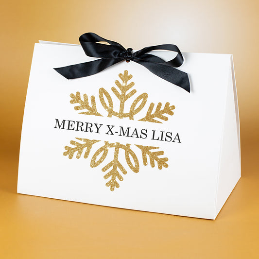 Sehr große Geschenktasche mit goldener Schneeflocke und personalisiertem Text „Merry X-Mas Lisa“, vor goldenem Hintergrund präsentiert.