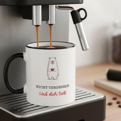 Keramiktasse mit niedlichem Bären und Herz-Spruch unter einer Kaffeemaschine befüllt.