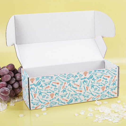 Geöffnete Geschenkbox mit farbigem Werkzeug-Muster und Deko auf gelbem Hintergrund mit WeintraubenDeko.