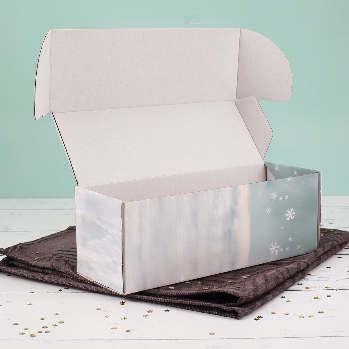 Geöffnete Flaschenverpackung mit winterlichem Wichtelmotiv, liegend auf dunklem Tuch