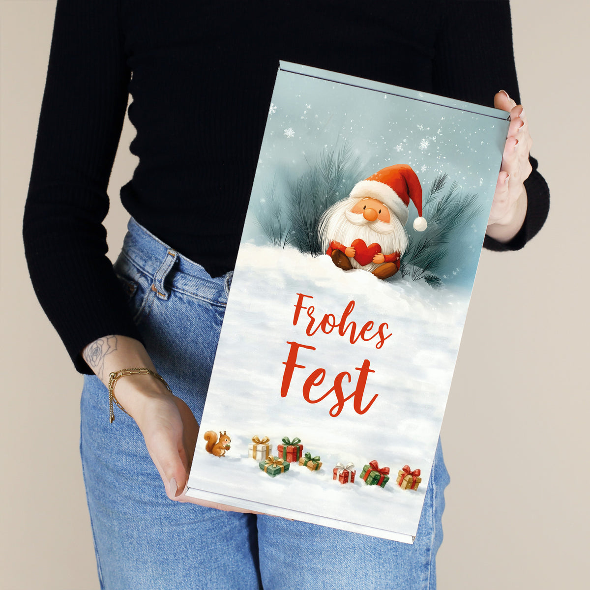 Person hält Geschenkbox „Frohes Fest“ mit Wichtelmotiv vor neutralem Hintergrund