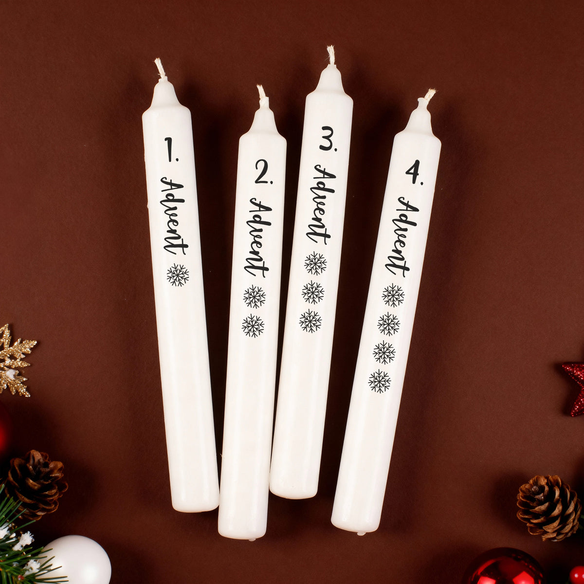 Adventskerzen-Set mit vier weißen Stabkerzen, beschriftet mit 1. bis 4. Advent und Schneeflocken, auf braunem Hintergrund.