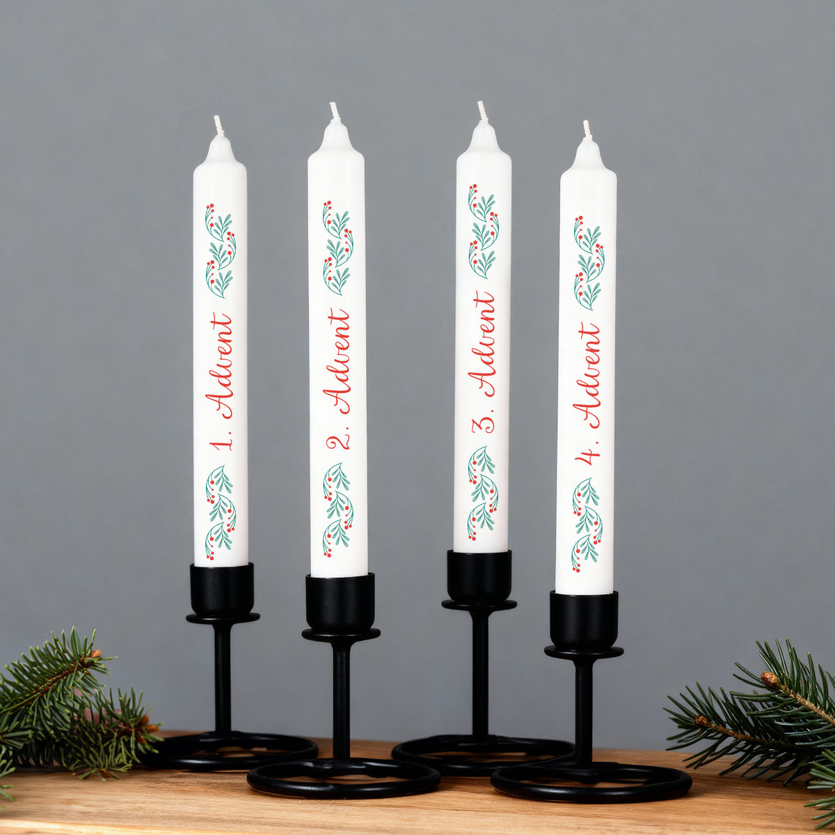 Adventskerzen-Set in schwarzen Kerzenhaltern, weiße Stabkerzen mit Zweigmotiv und Beschriftung 1.–4. Advent vor grauem Hintergrund.