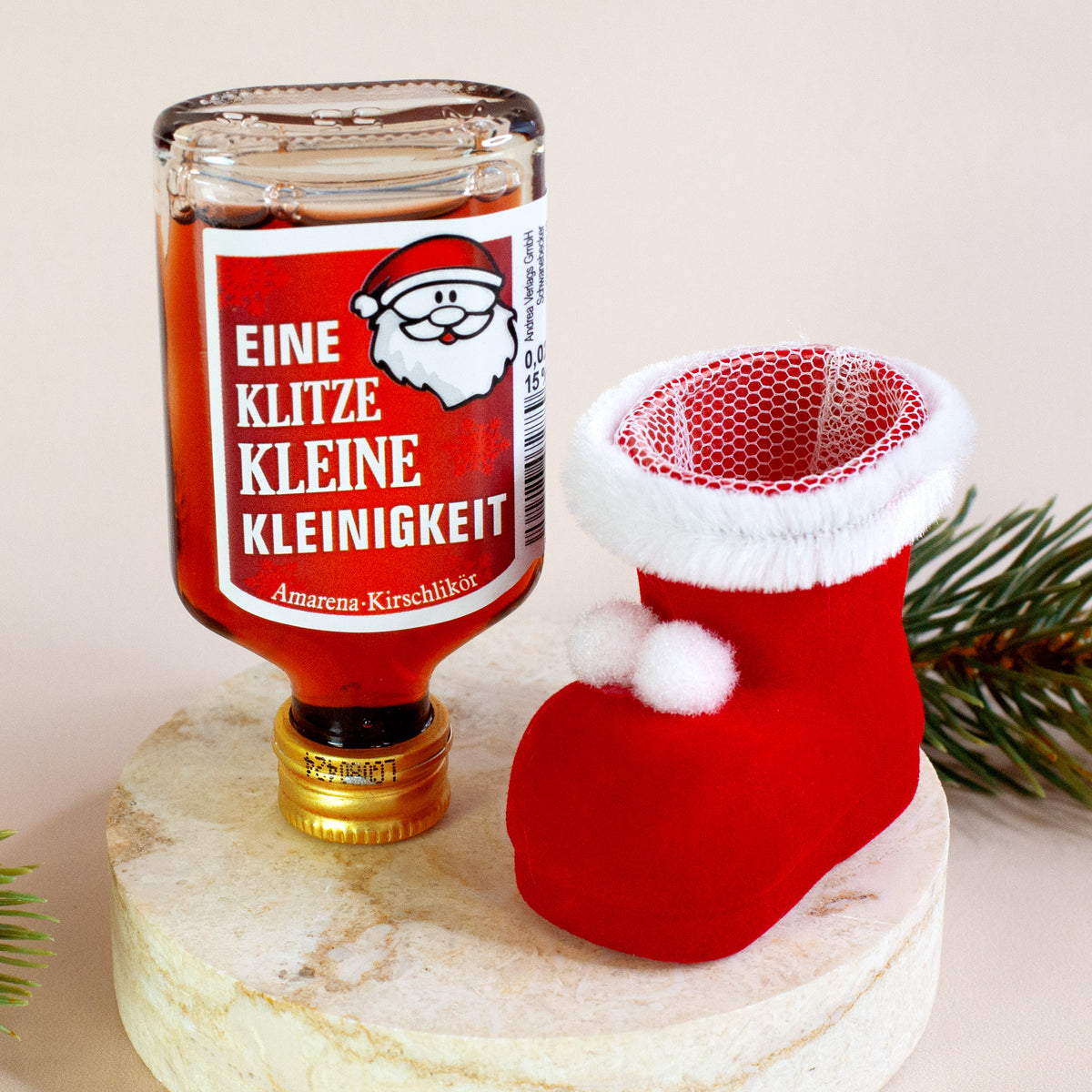 Likörflasche mit dem Spruch „Eine klitzekleine Kleinigkeit“ steht kopfüber vor einem leeren roten Nikolausstiefel. Die Szene ist liebevoll dekoriert mit natürlichen Elementen.