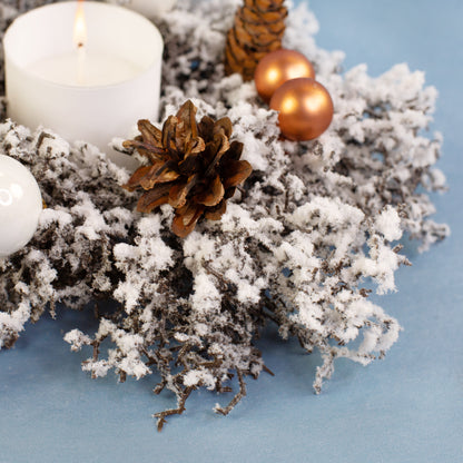 Nahaufnahme des verschneiten Adventskranzes mit Tannenzapfen und Schneestruktur