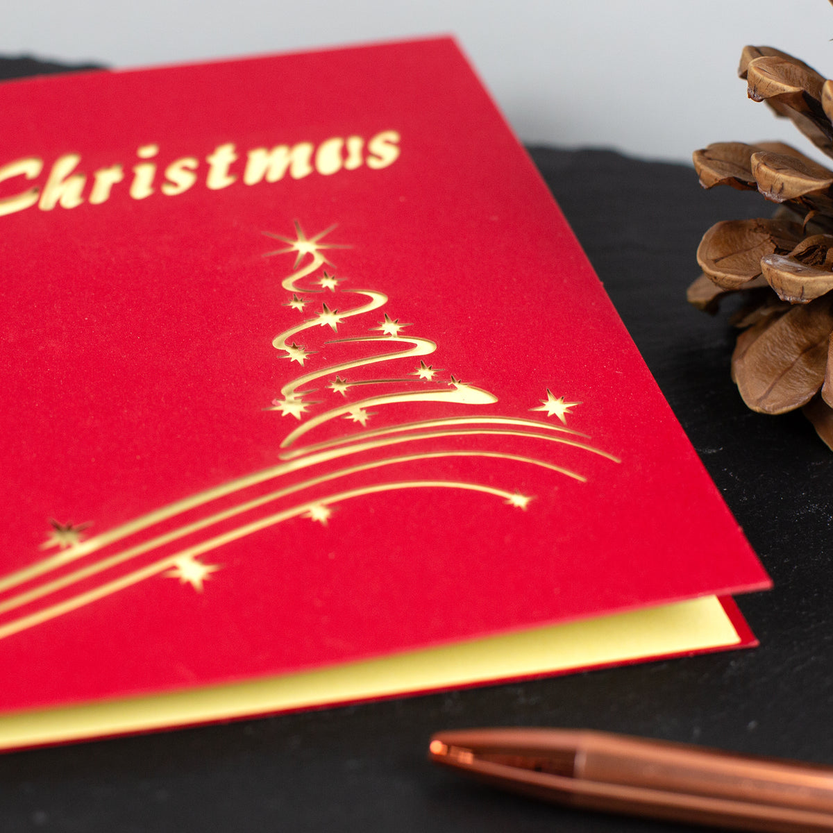 Detailaufnahme der Vorderseite der roten Weihnachtskarte mit goldenem Tannenbaum-Design und „Merry Christmas“-Schriftzug.
