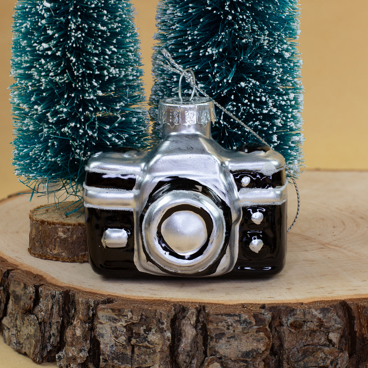 Schwarz-silberne Kamera als Retro Glas Weihnachtsbaumschmuck zwischen verschneiten Tannen