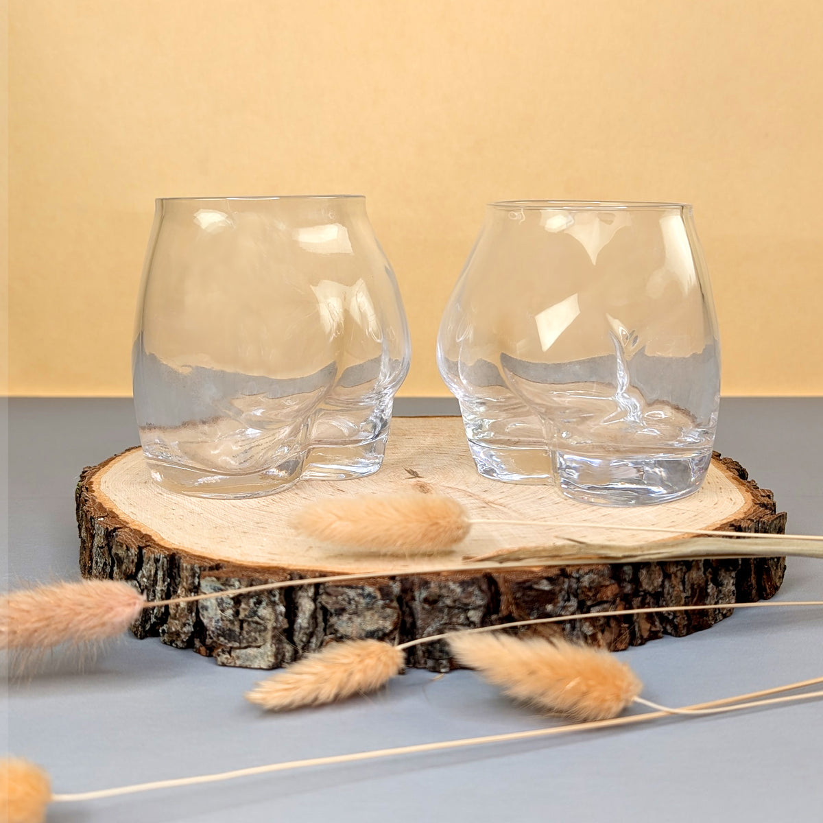 Zwei leere Trinkgläser im Gesäß-Design auf Holzscheibe arrangiert