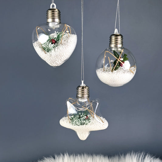 Drei beleuchtete Christbaumkugeln mit Styroporkugeln, Zweigen und roten Beeren vor grauem Hintergrund.