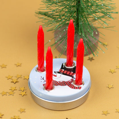 Mini-Adventskranz mit vier eingesetzten roten Kerzen im Schneemann-Design, vor einem kleinen Weihnachtsbaum und goldenen Stern-Konfetti.