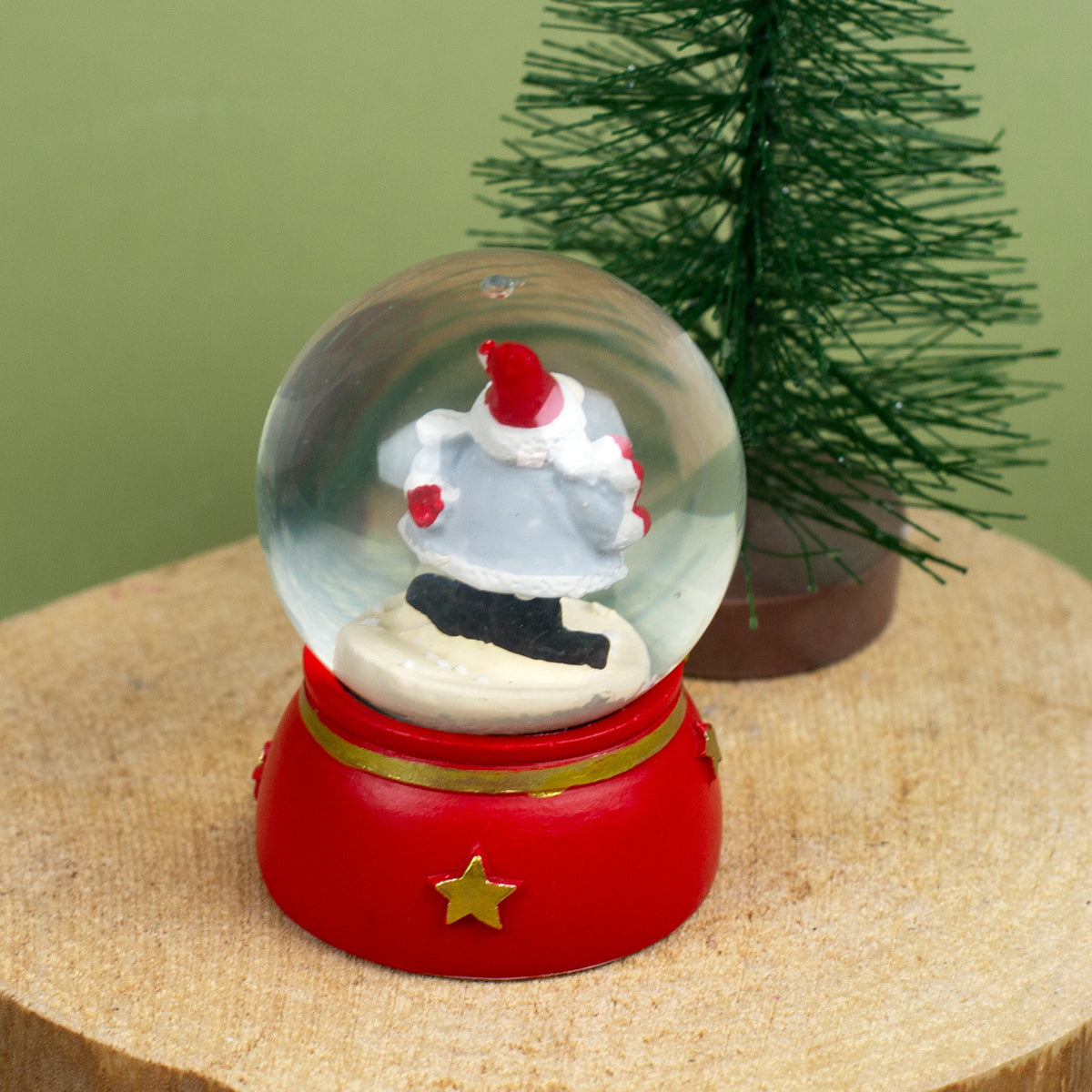 Schneekugel mit Weihnachtswichtel, der ein rotes Herz in den Händen hält, auf Holzuntergrund dekoriert