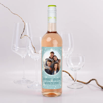 Personalisierte Roséweinflasche mit Schneeflocken-Etikett, eigenem Foto und Weihnachtsgruß – Szene mit Gläsern
