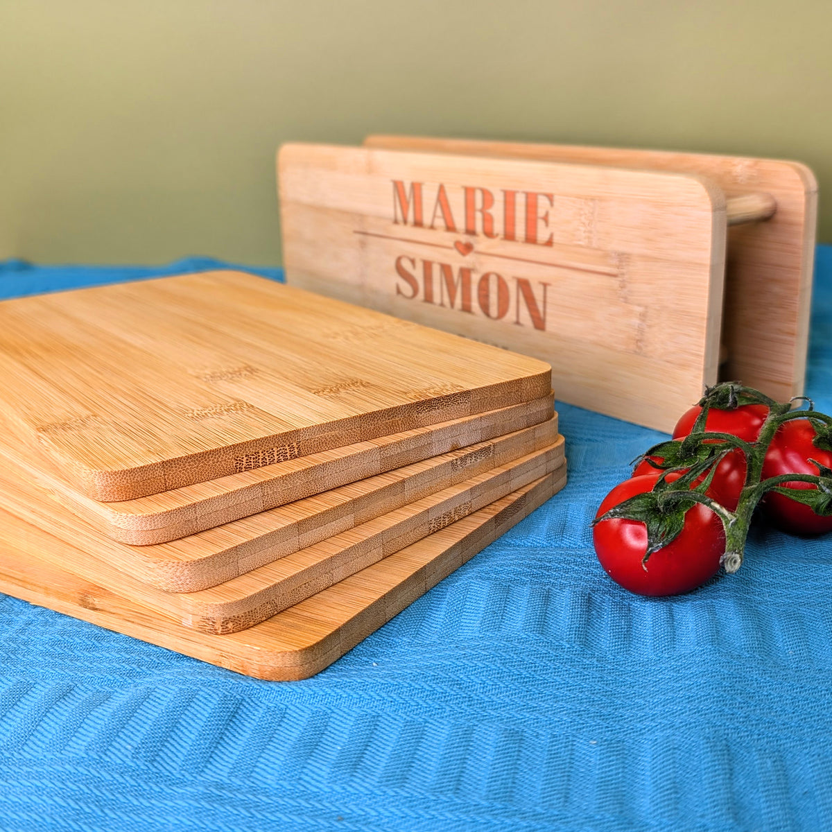 Fünf Bambusbrettchen gestapelt, im Hintergrund gravierter Ständer mit „Marie & Simon“ und Tomaten