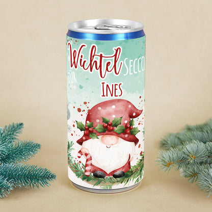 Personalisierte Secco-Dose mit Wichtelmotiv, roter Mütze, Mistelkranz und Name Ines, dekoriert mit Tannenzweigen als Weihnachtsgeschenk.