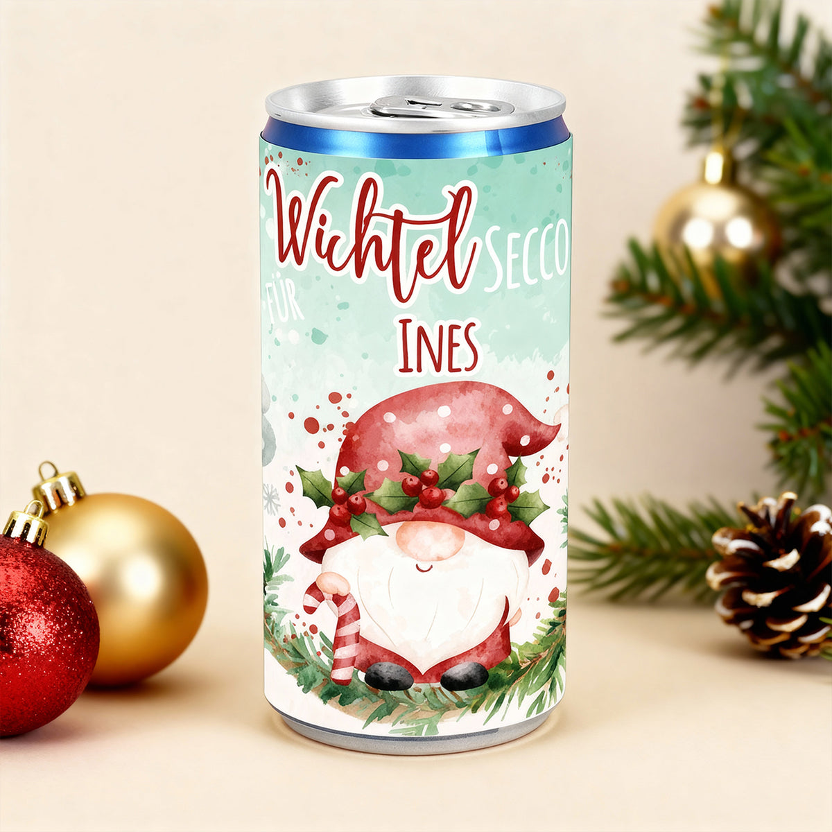 Personalisierte Secco-Dose mit Wichteldesign und Name Ines, Weihnachtsdeko mit Christbaumkugeln im Hintergrund.