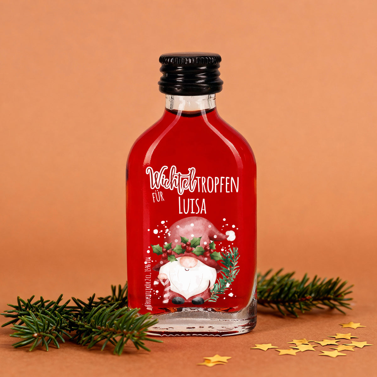 Mini-Schnapsflasche mit rotem Fruchtlikör, Wichtelmotiv und personalisiertem Namen, dekoriert mit Tannenzweigen.