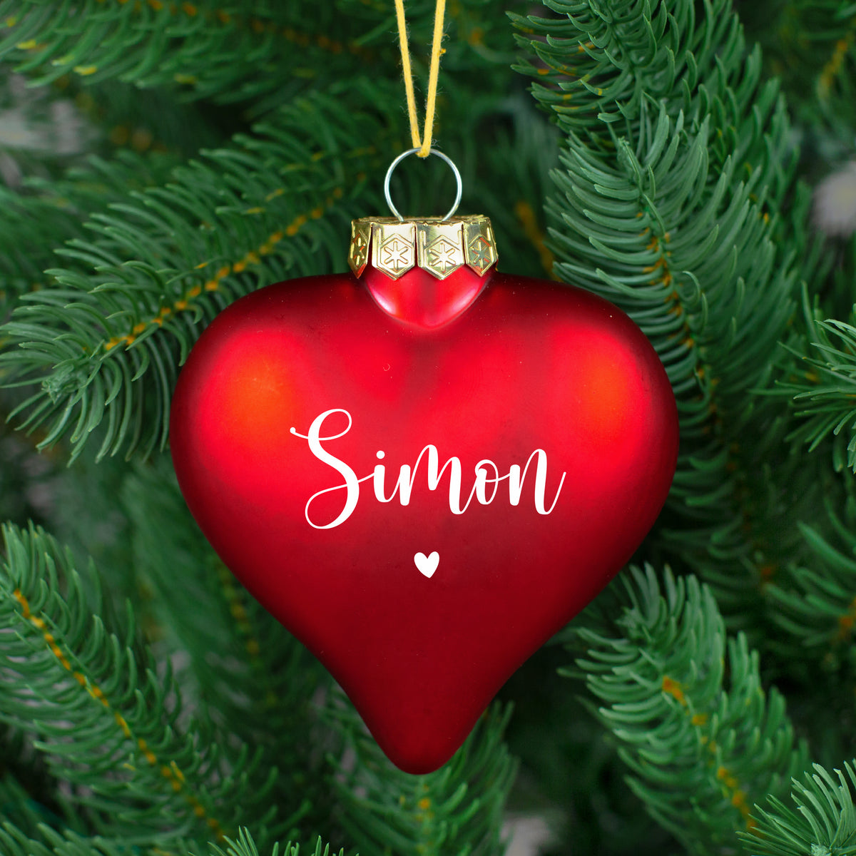 Glänzende rote Herz-Weihnachtskugel mit Name „Nicole“ auf weißem Fell, Tannenzweig im Anschnitt.