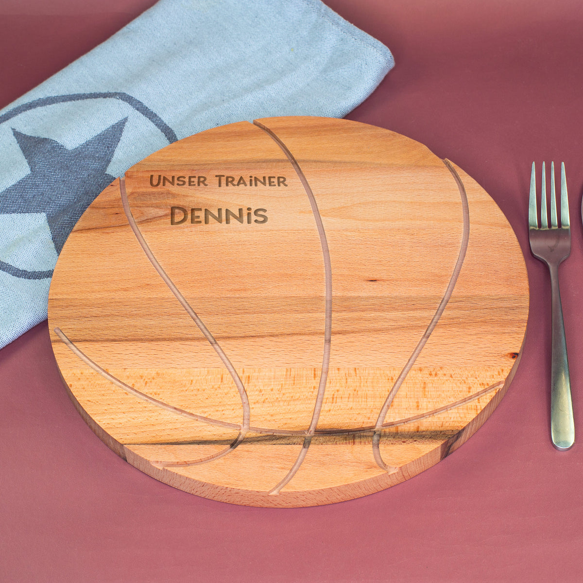 Personalisierbares Holzbrett in Basketballform mit Gravur Unser Trainer Dennis, dekorativ präsentiert