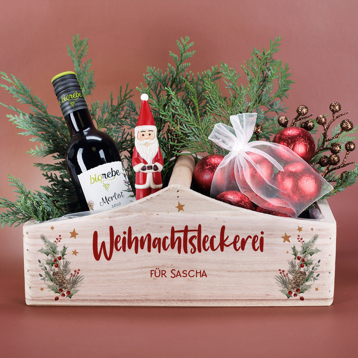 Gefüllter Weihnachtskorb mit Winterbouquet-Motiv, roten Kugeln, Wein und Tannengrün als Geschenkarrangement.