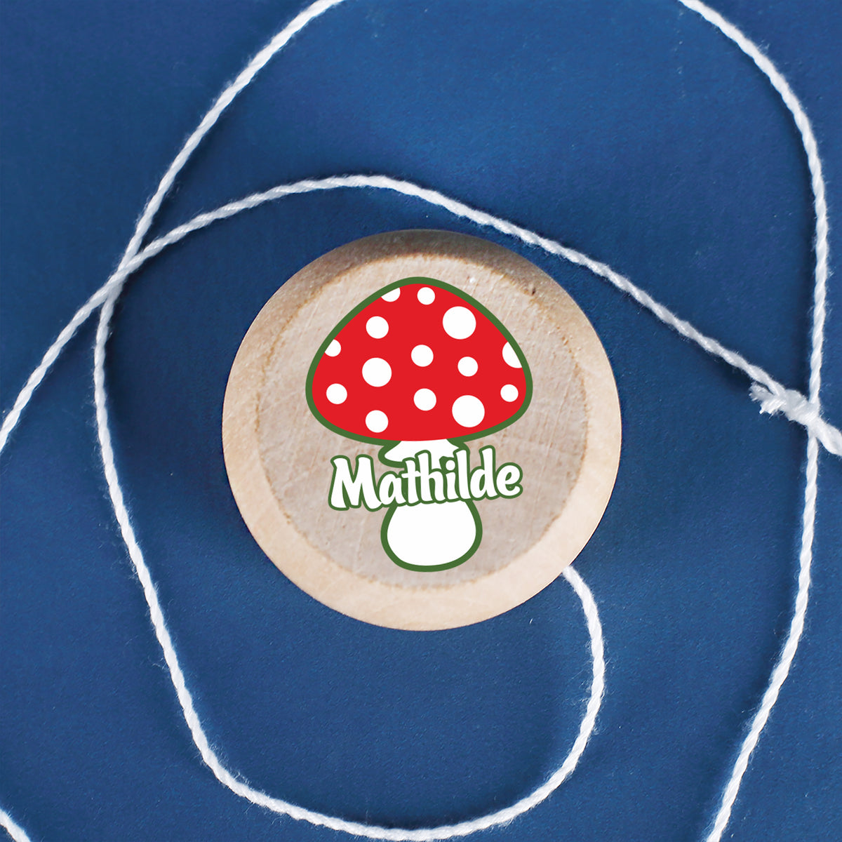Yo-Yo mit Fliegenpilz-Motiv und Wunschname aus Holz auf blauem Hintergrund liegend