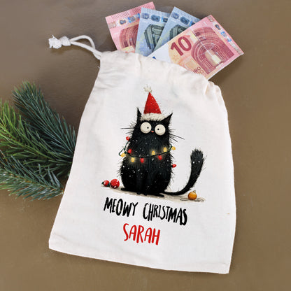 Stoffbeutel mit Katzenmotiv „Meowy Christmas – Sarah“, befüllt mit Geldscheinen und Tannenzweig daneben