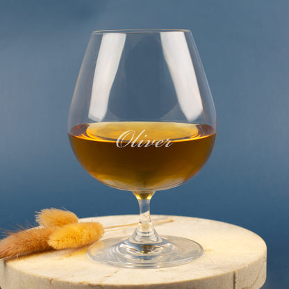 Leonardo Cognacglas mit Gravur „Oliver“ – auf hellem Holzuntergrund mit Trockenblumen, blauer Hintergrund.