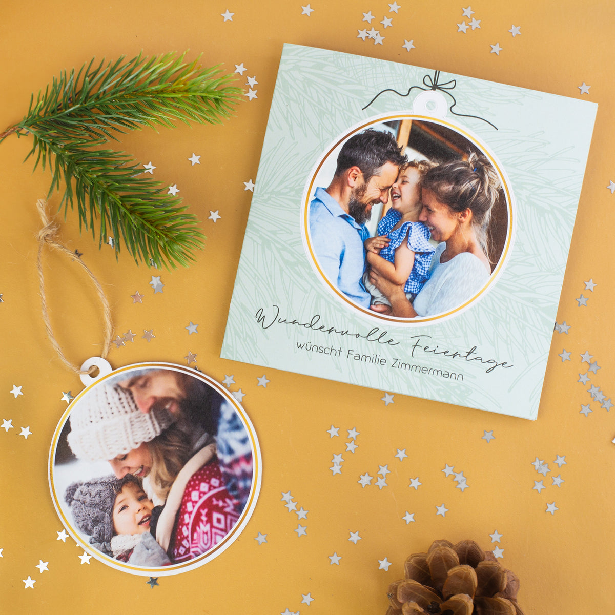 Quadratische Weihnachtskarte mit herausnehmbarer runder Fotokugel und zweitem Foto, dekoriert mit Tannenzweig, Sternkonfetti und Tannenzapfen auf goldenem Hintergrund