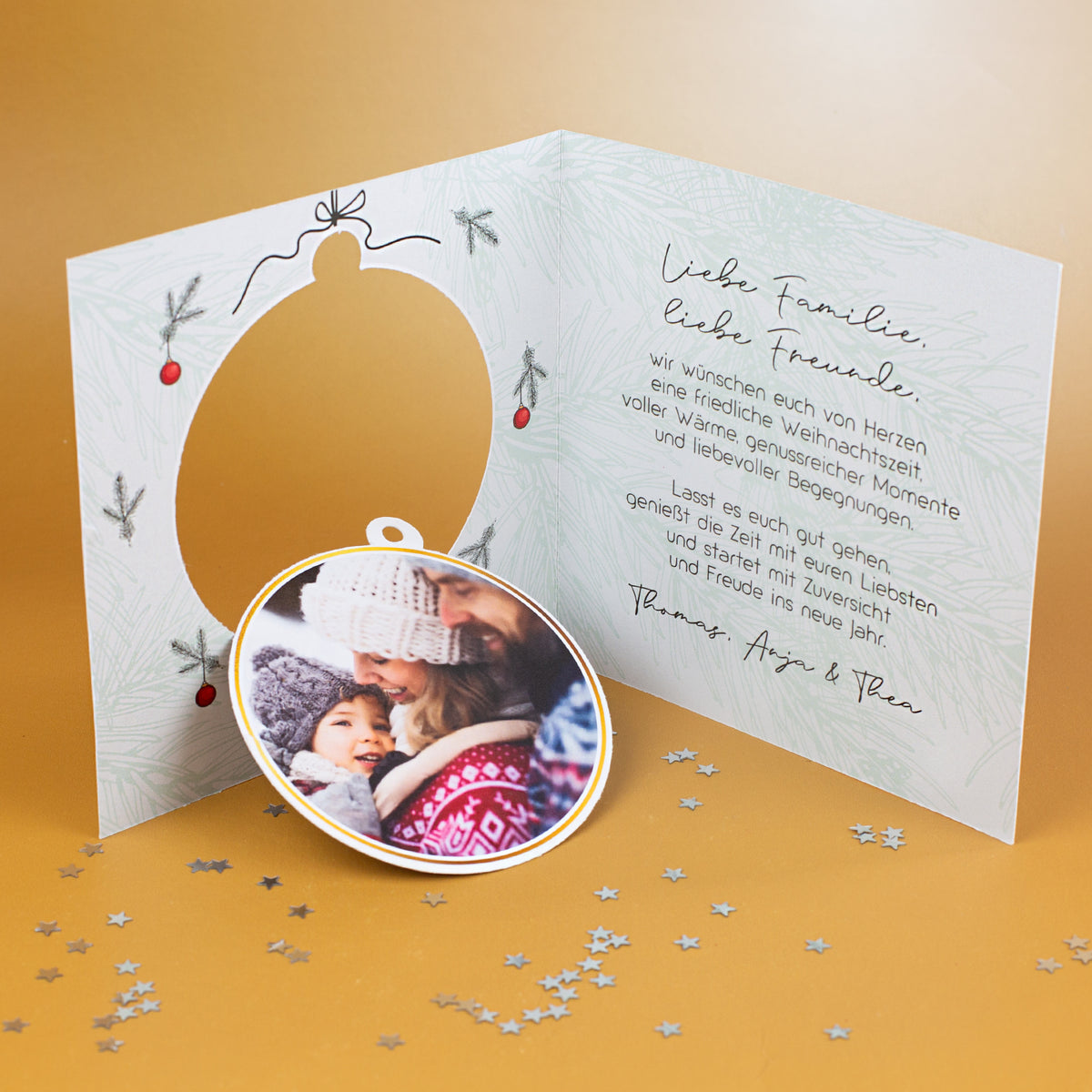 Geöffnete Weihnachtskarte mit kreisförmiger Aussparung links, herausgenommener Fotokugel im Vordergrund und gedrucktem Weihnachtsgrußtext auf der rechten Innenseite