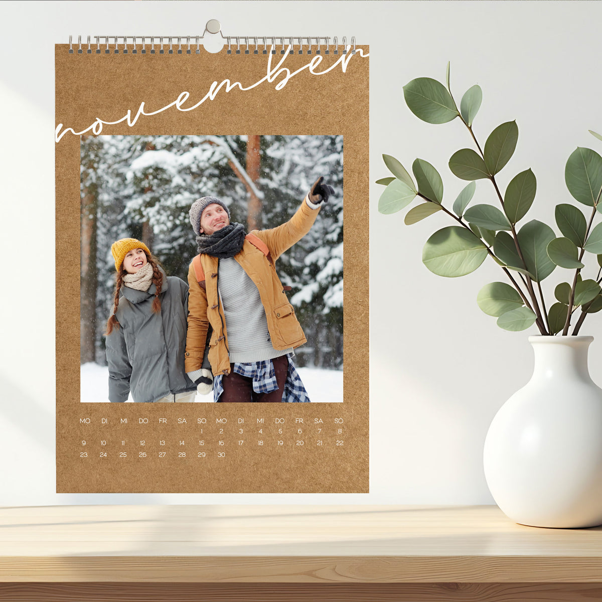 Foto-Wandkalender für November in natürlicher Kraftpapier-Optik, mit Winterfoto eines Paares im Schnee, dekoriert auf einem hellen Sideboard.