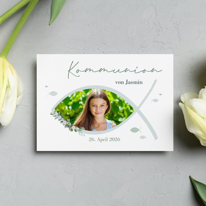 Personalisierte Einladungskarte zur Kommunion mit christlichem Fischsymbol (Ichthys). Vorderseite mit individuellem Foto, sanften Grüntönen und stilvollen Blätterelementen.