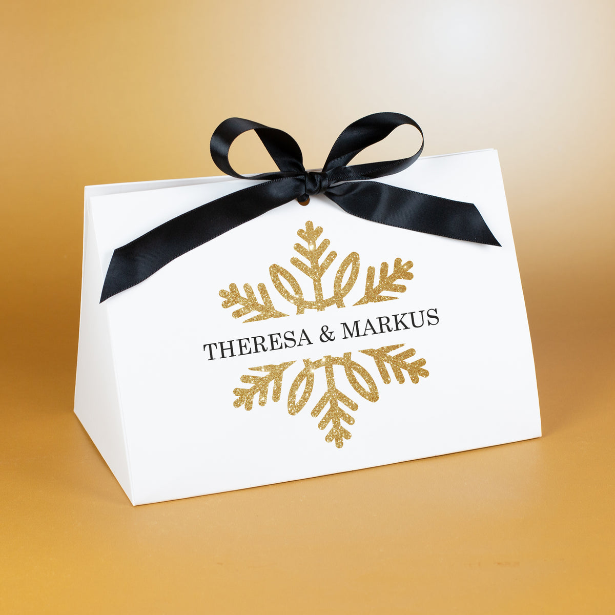 Große Geschenktasche mit goldfarbener Schneeflocke und personalisierter Aufschrift „Theresa & Markus“, edel vor warmem Hintergrund platziert.