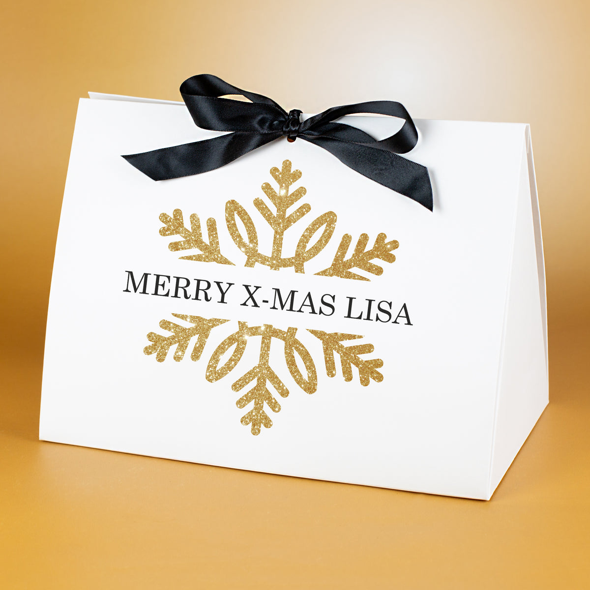 Sehr große Geschenktasche mit goldener Schneeflocke und personalisiertem Text „Merry X-Mas Lisa“, vor goldenem Hintergrund präsentiert.