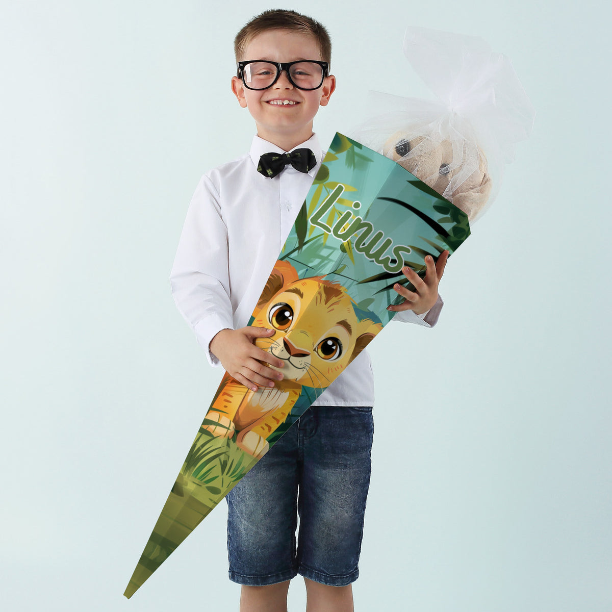 Junge im weißen Hemd und Fliege hält stolz eine Dschungel-Schultüte mit Löwenmotiv und Name „Linus“.