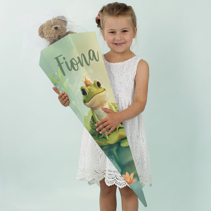 Mädchen in weißem Kleid lächelt mit einer großen Zuckertüte mit dem Namen "Fiona" und Frosch-Motiv