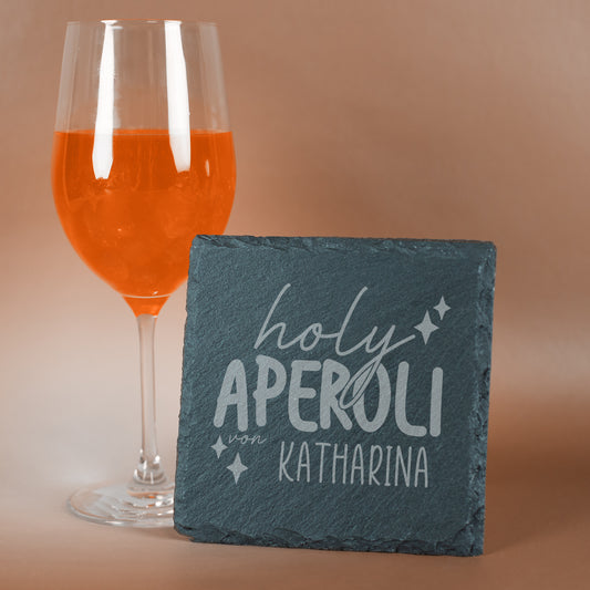 Schiefer-Untersetzer mit Gravur „holy Aperoli von Katharina“ aufgestellt neben einem Aperitif fotografiert