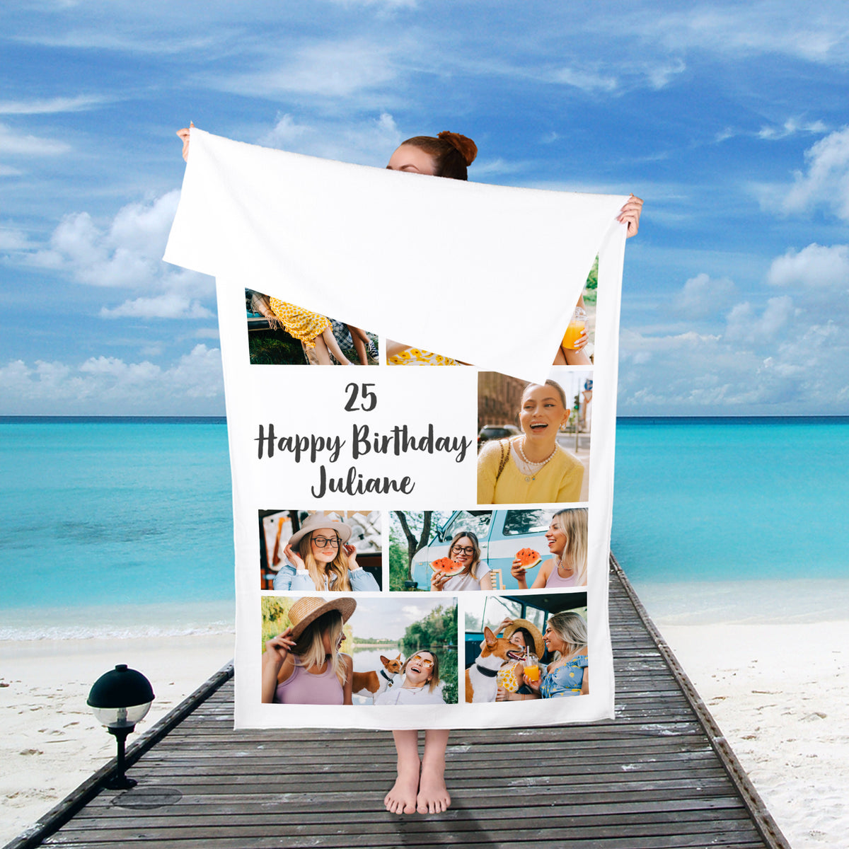 Person steht am Strand und hält ein individuell bedrucktes Badetuch mit Foto und Text von hinten in die Höhe – sommerliche Kulisse mit Meerblick.