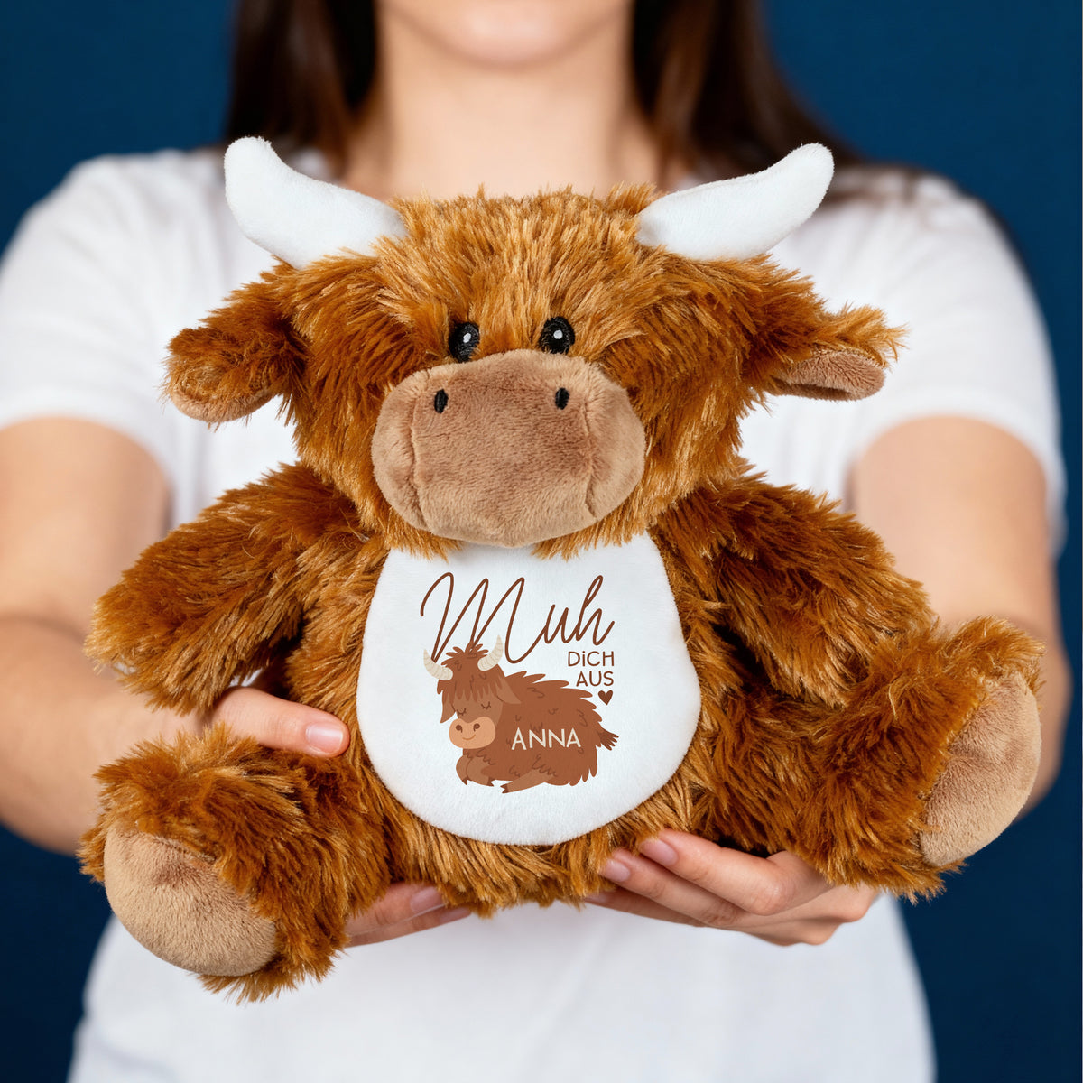 Person hält eine braun-weiße Kuscheltier-Kuh mit dem Aufdruck „Muh dich aus“ und dem personalisierten Namen „Anna“ in den Händen