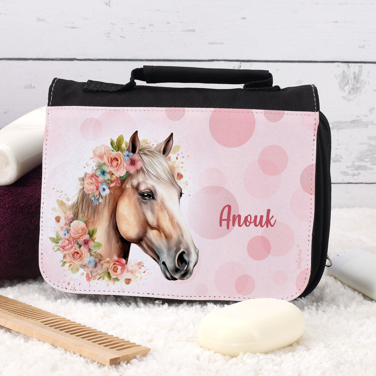 Schwarze Waschtasche mit Blumen-Pferdemotiv und Name „Anouk“ auf Teppich mit Seife und Kamm