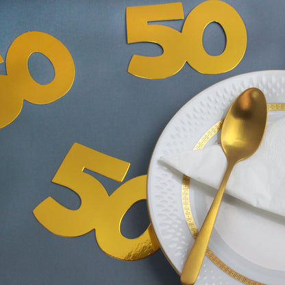 Goldene Jumbo-Konfetti Zahl 50 als Streudeko auf grauem Hintergrund neben Teller